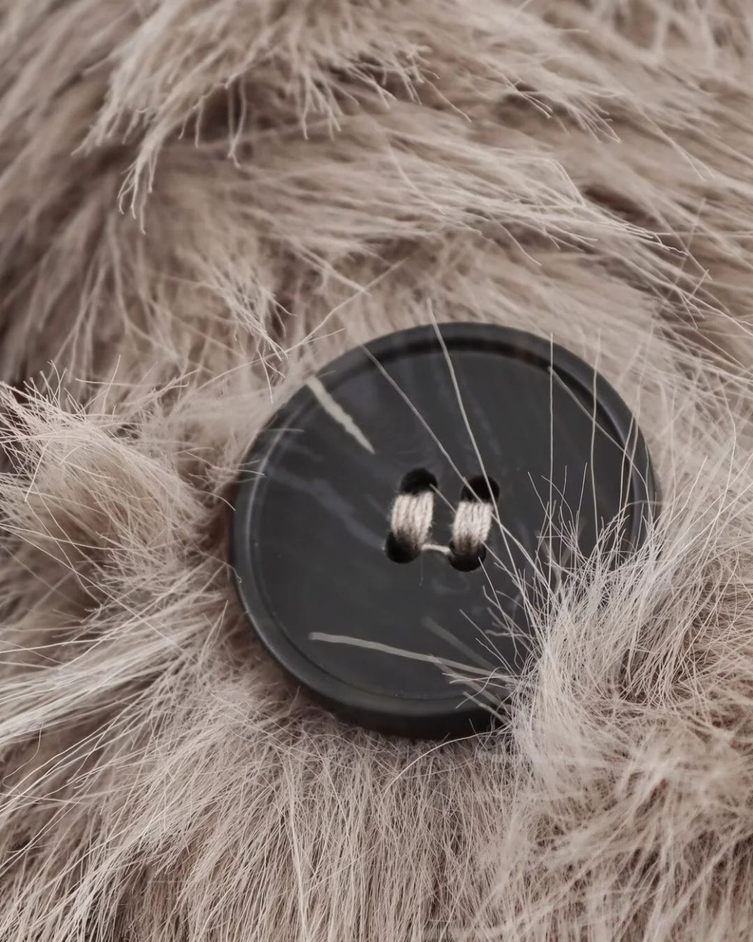 Detailaufnahme des Knopfverschlusses eines khaki Faux-Fur-Mantel